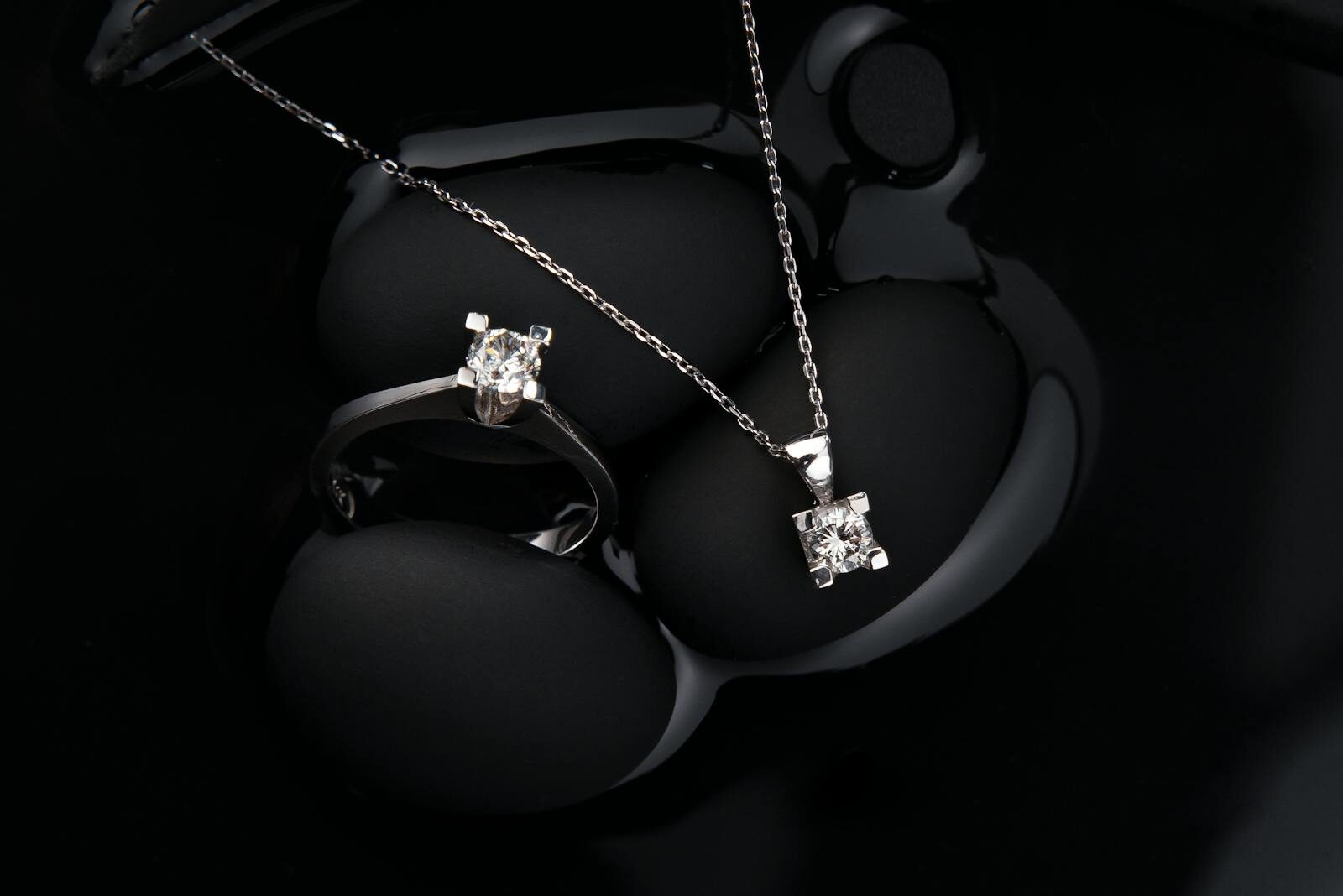 Luxurious silver diamond ring and pendant necklace on a black background, showcasing elegance and sophistication.