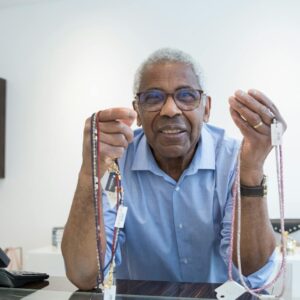 Senior man smiling and showcasing necklaces in a bright, modern store.